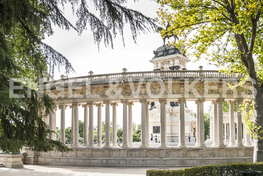 Exterior view of the Monument to Alfonso XII in El Retiro Park, Madrid. Stone columns surround a statue on a plinth.