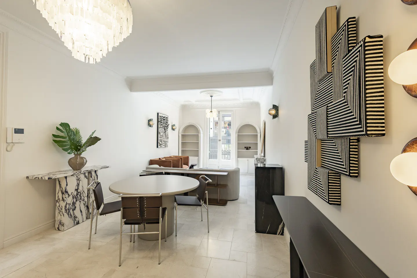 Bright, modern living space with white walls, marble accents, and geometric art. A round table and chairs sit near a marble console table with a plant.