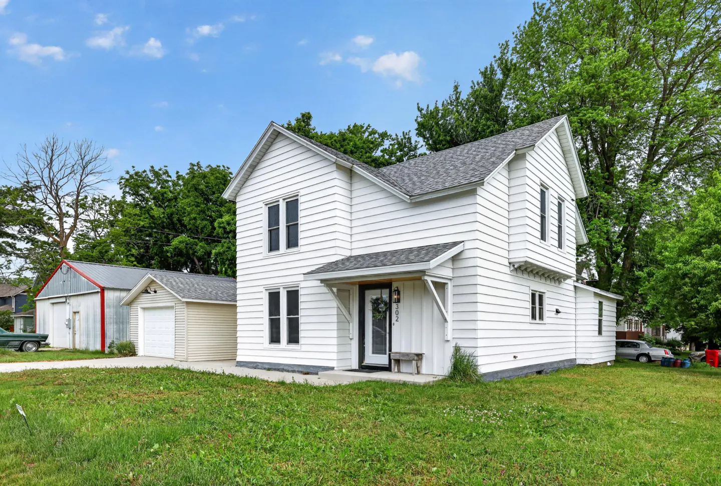 Two-story white house with horizontal siding, a covered front porch, and a detached garage on a grassy lot.