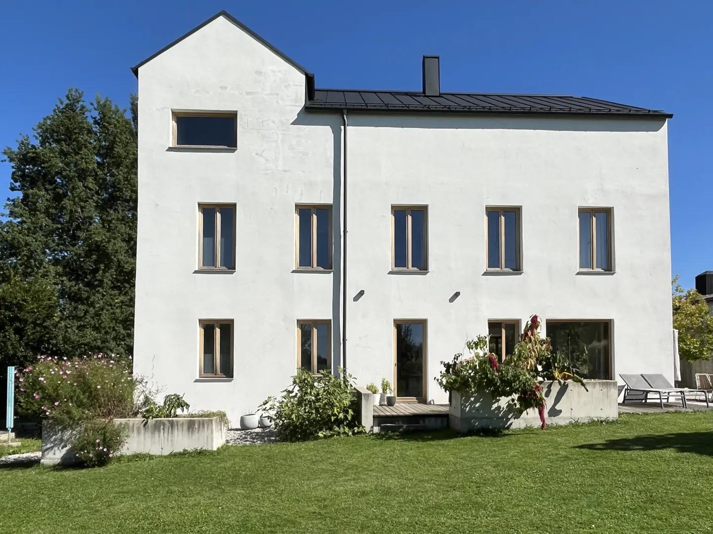 A three-story white house with a black roof and green lawn under a blue sky.