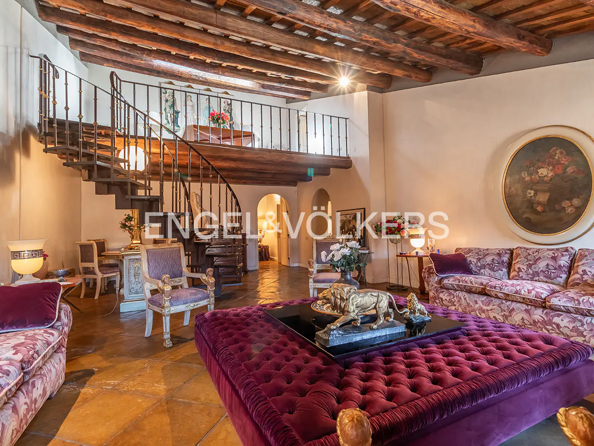 Interior view of a living room with a spiral staircase, a purple ottoman with lion statues, and a floral sofa.