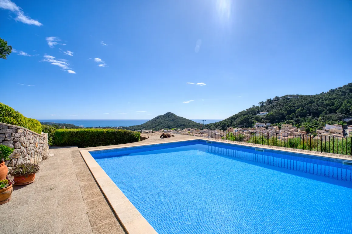 Outdoor pool with blue tiles, stone patio, and mountain view under a sunny blue sky.