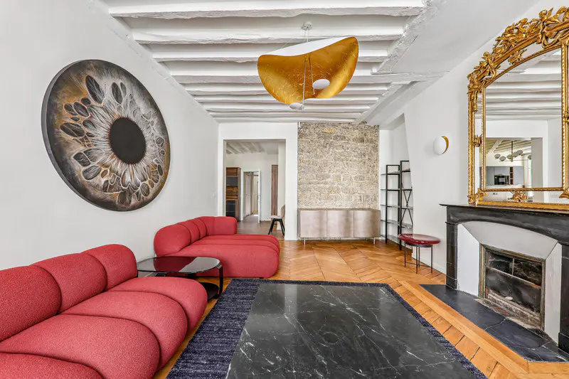 Living room with red sofas, black marble table, and a large eye art piece on the wall. A gold mirror hangs above the fireplace.