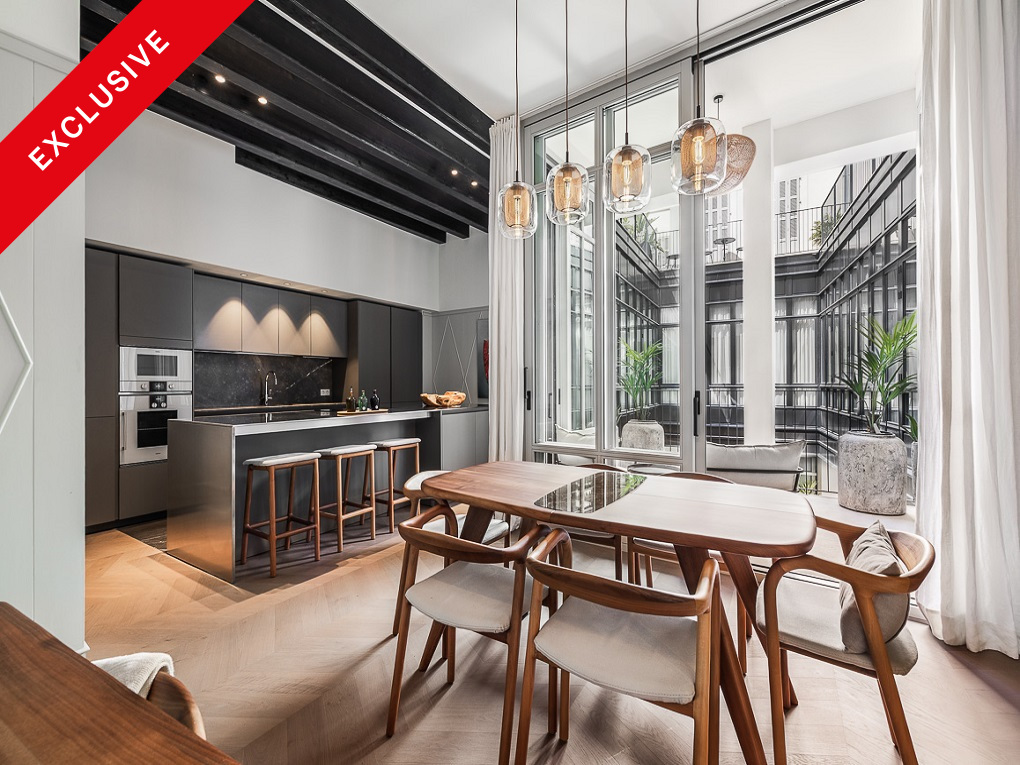 Modern kitchen and dining area with dark cabinets, wooden table, and floor-to-ceiling windows overlooking a courtyard. [AI-generated text]