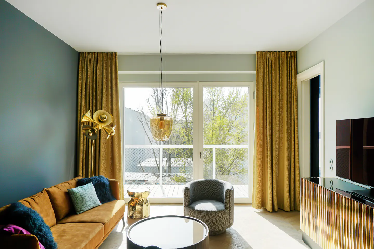 Living room with brown sofa, blue pillows, gold accents, and a large window with gold curtains.