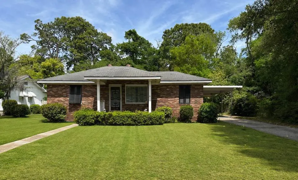 A single-story brick house with a green lawn and trees in the background.