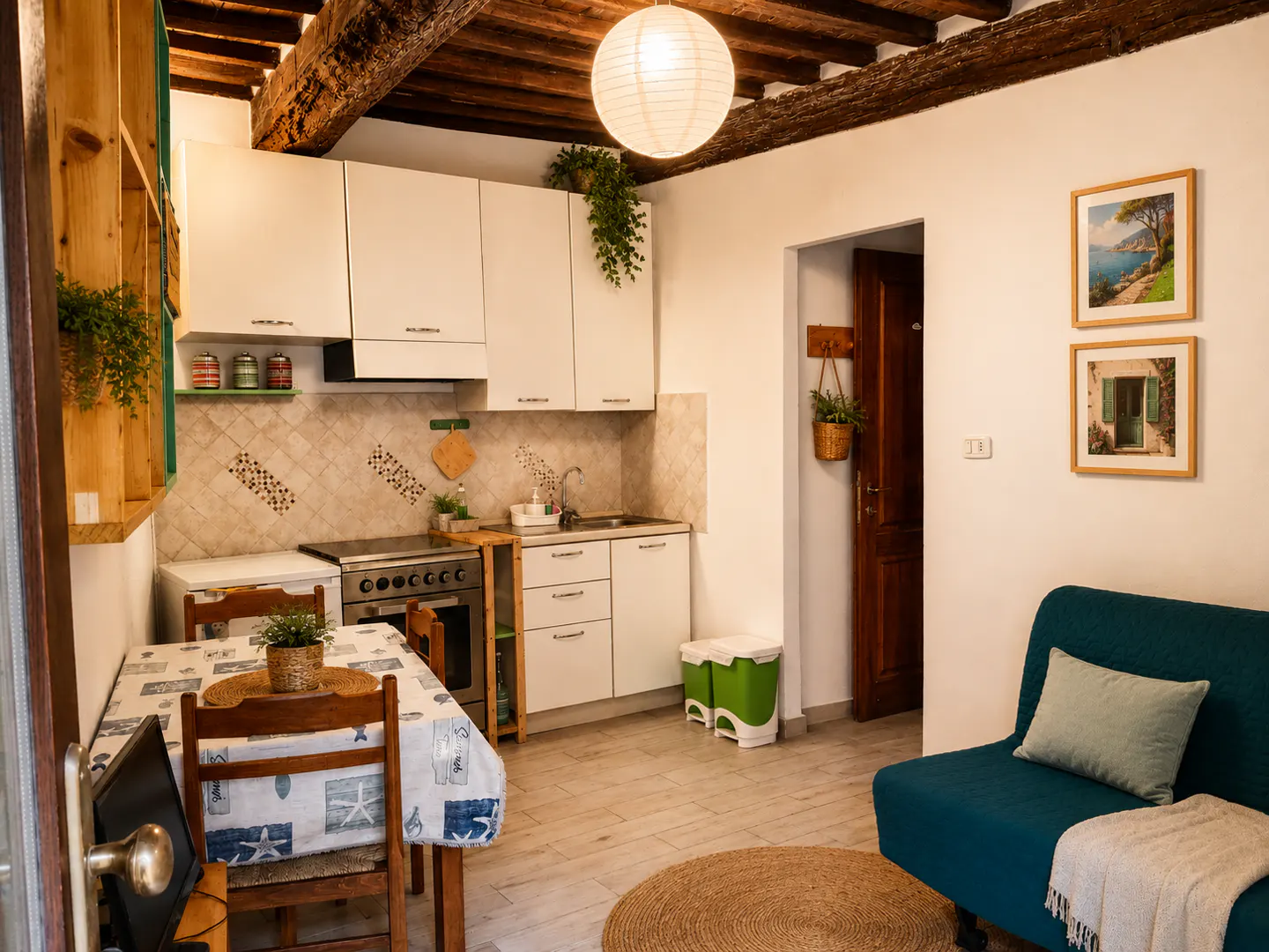 Cozy apartment interior with white cabinets, wooden beams, and a teal sofa. A dining table sits near the kitchen area. Artwork adorns the walls.