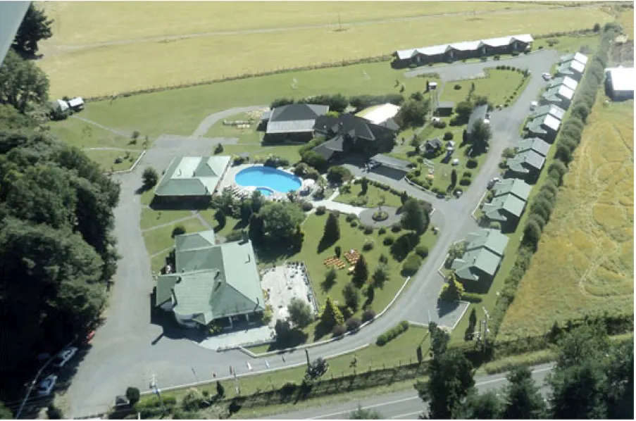 Aerial view of a resort with a blue pool, green roofs, and surrounding fields.