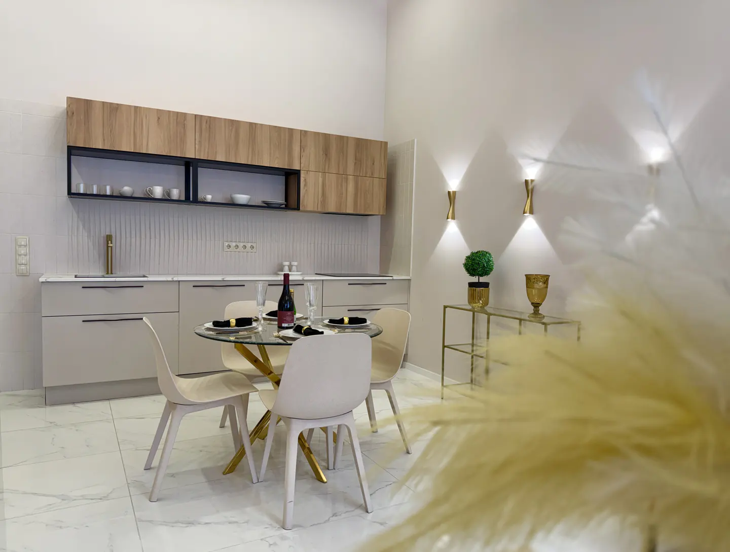 A modern kitchen with a round glass table set for four, a wine bottle, and light wood cabinets.
