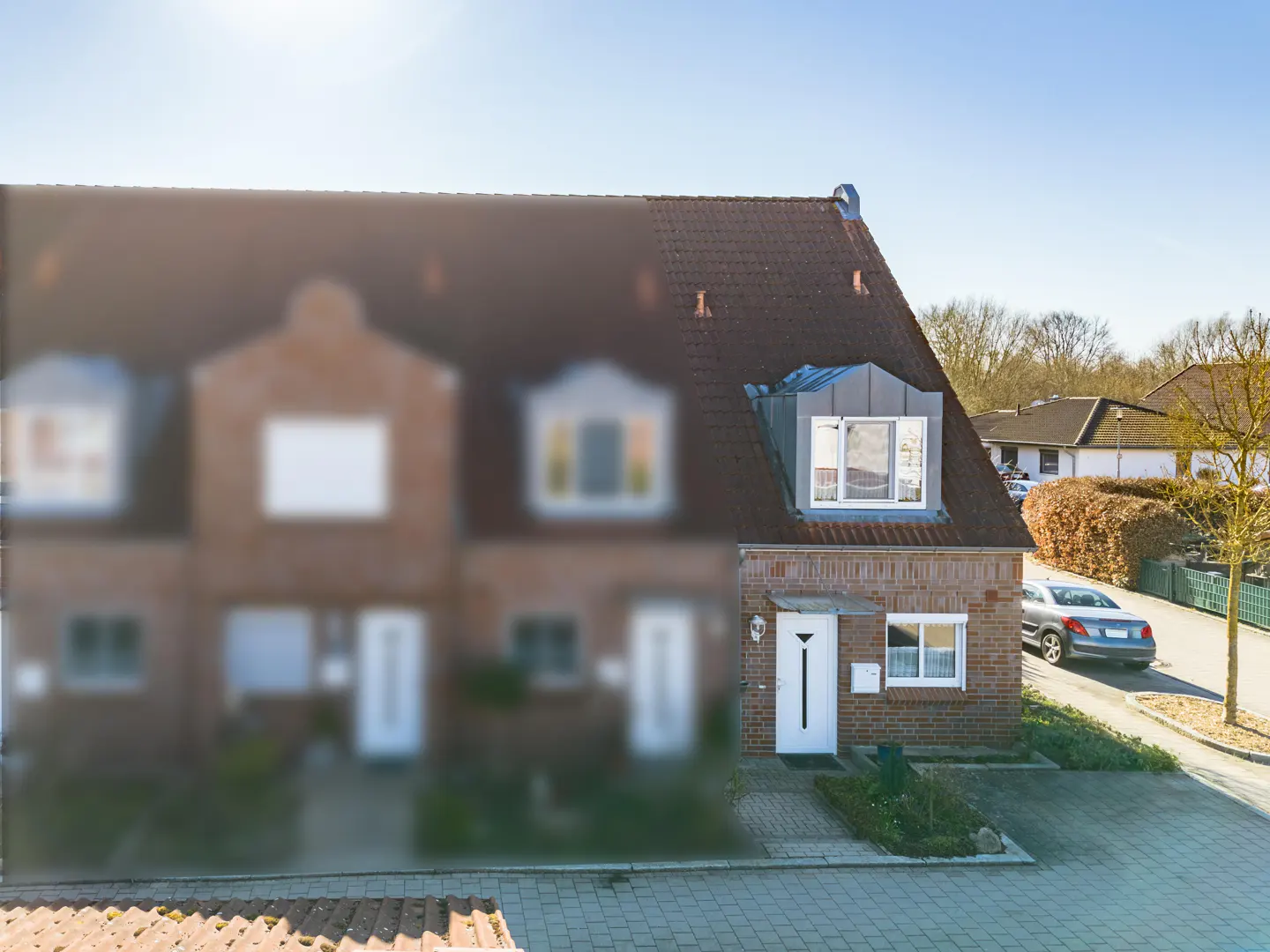 Brick townhouse with a red roof and white door. A silver car is parked on the street.