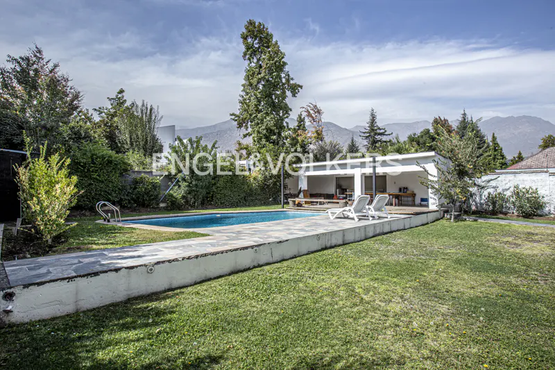 A backyard with a blue pool, two white lounge chairs, a white pergola, and green grass. Mountains are in the background.