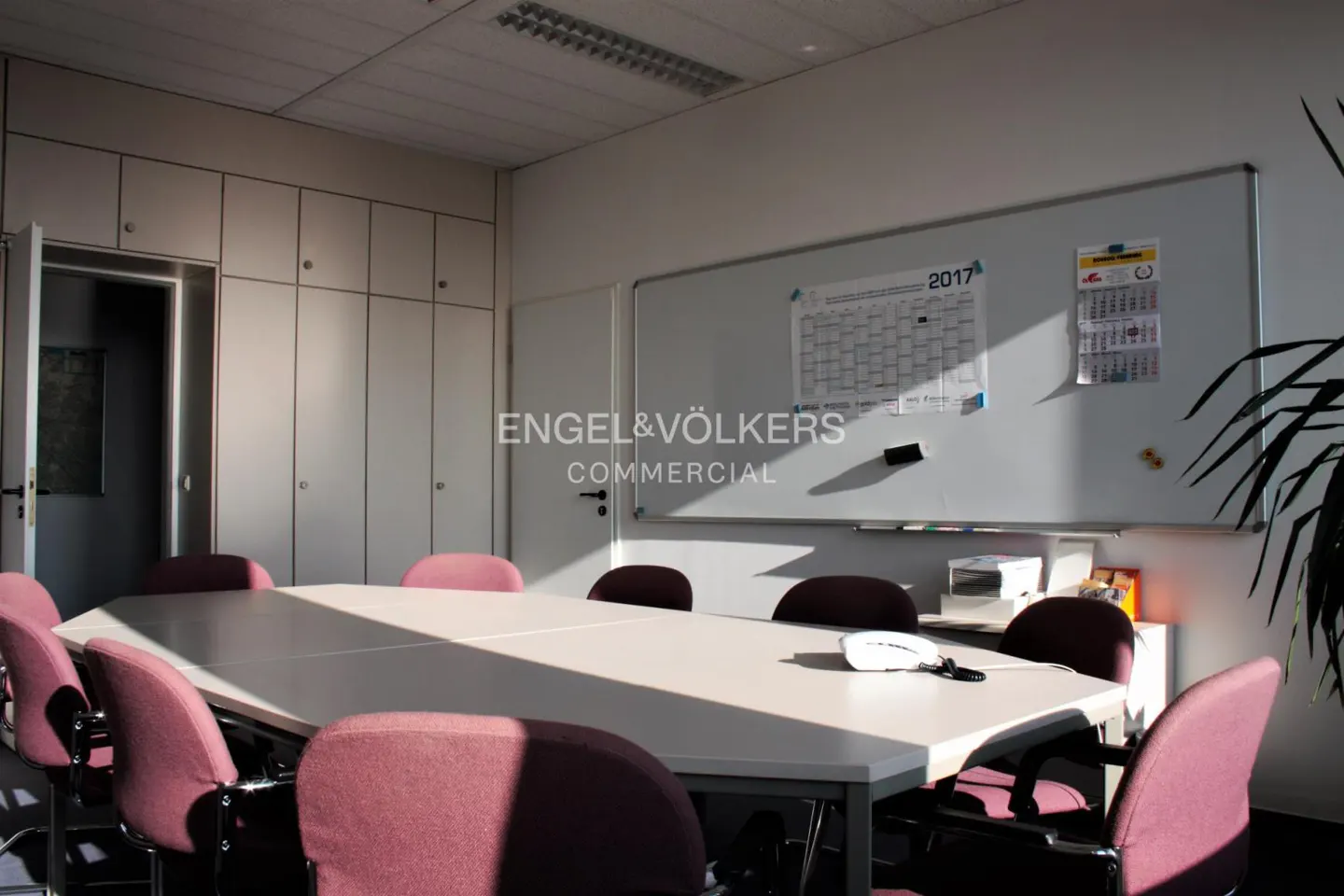 Conference room with a white table, maroon chairs, and a whiteboard with a calendar.