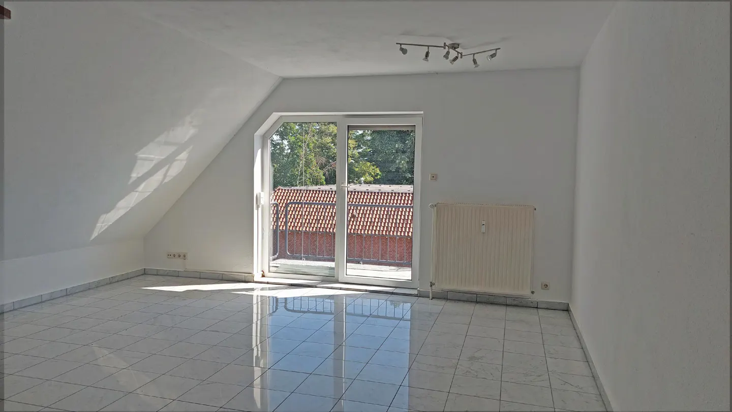 Bright, empty room with white walls, tiled floor, and sliding glass doors to a balcony. A radiator is on the wall.