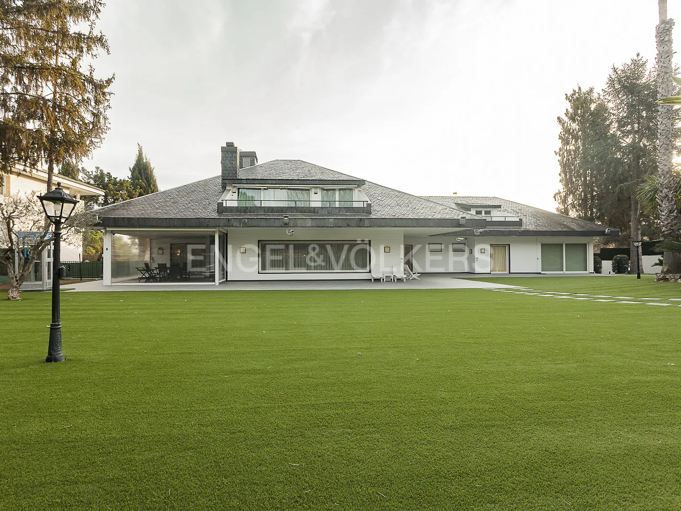 Wide shot of a modern white house with a gray roof and large green lawn. A black lamppost stands on the left.