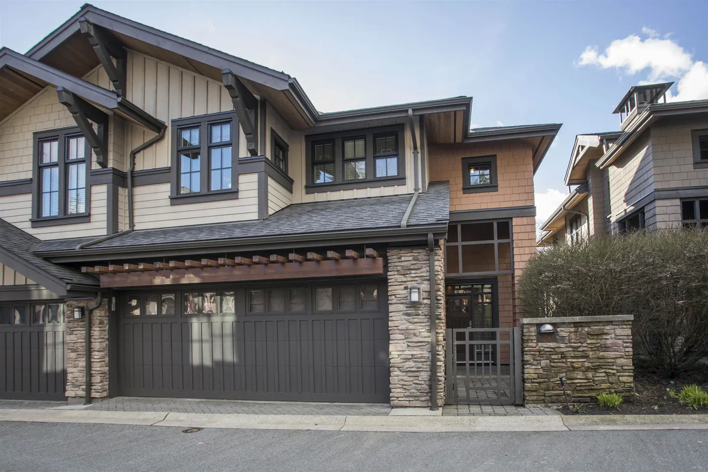 Exterior view of a two-story townhouse with a dark gray garage door and stone accents. The house has beige siding and black-framed windows.