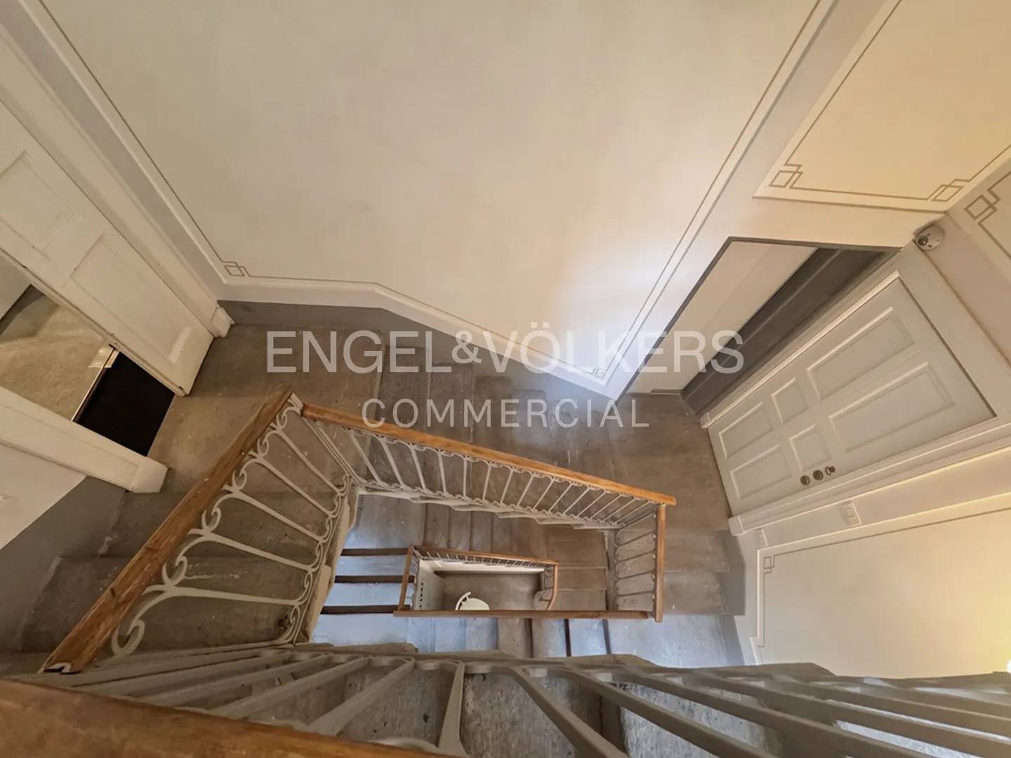 Looking down a winding staircase with white railings and wooden handrails in a building with white walls and ceiling.