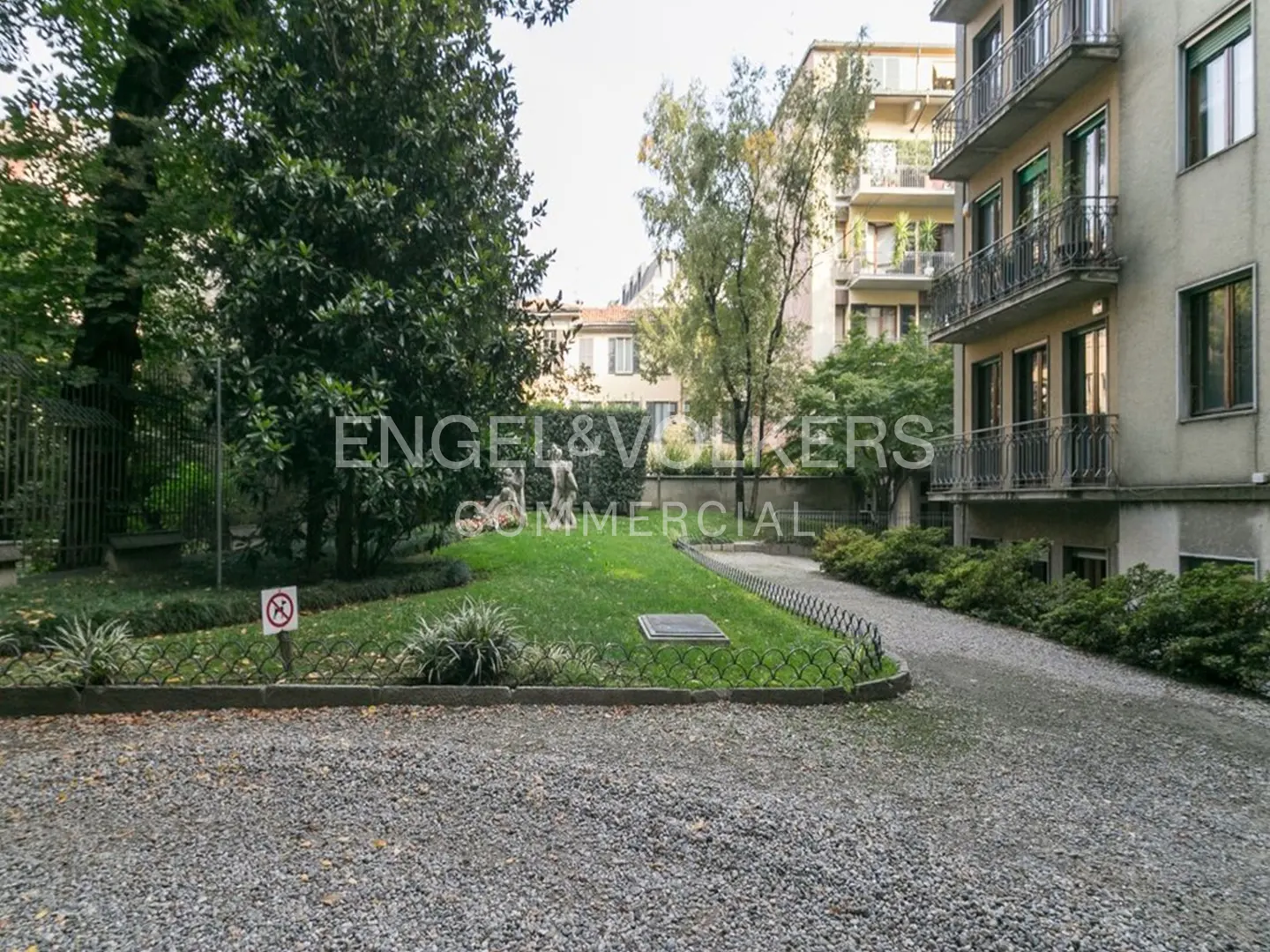 Exterior view of a building with a gravel driveway, lawn, trees, and an Engel & Volkers sign.