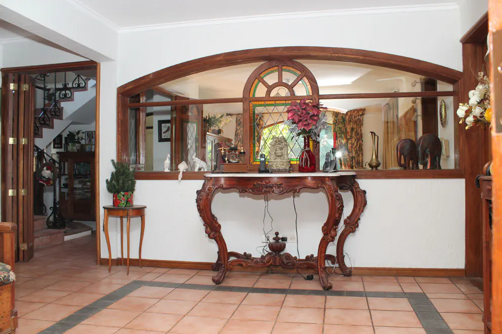 A foyer with a decorative wooden table, a large arched window, and terracotta tile flooring.