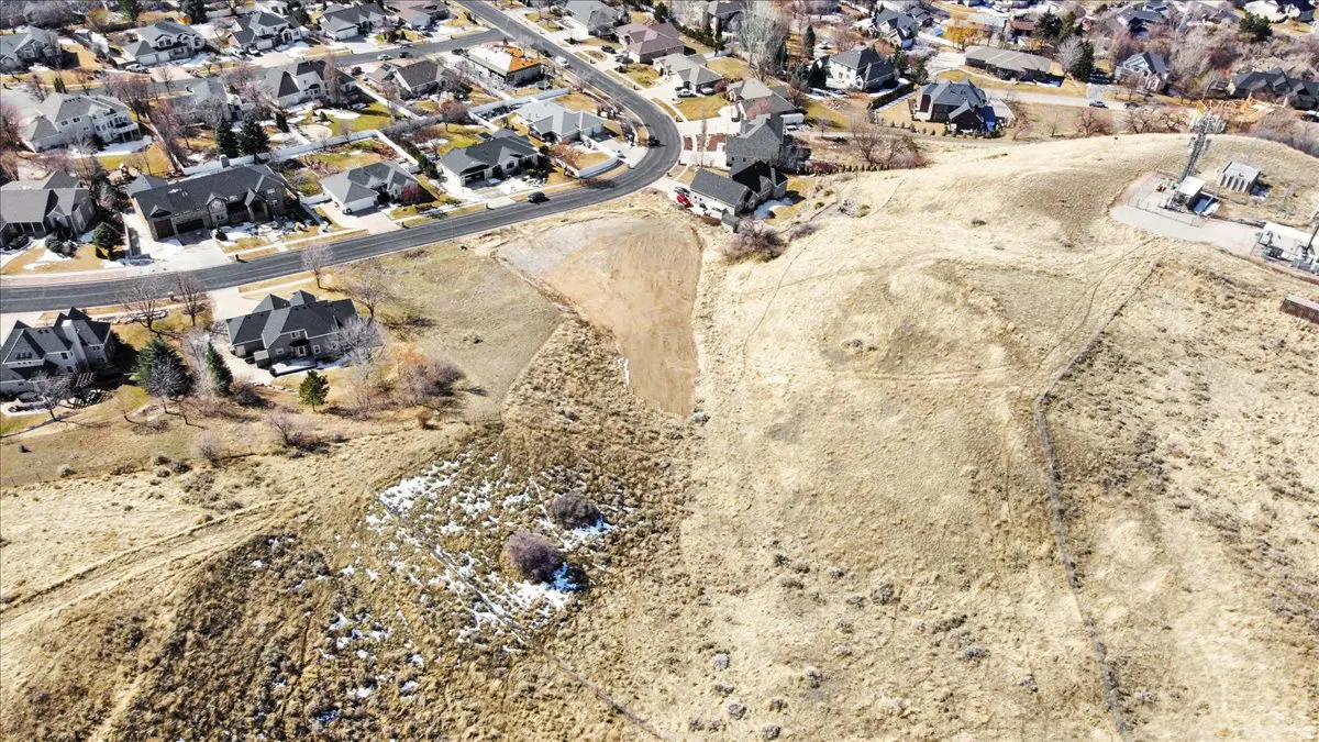 Aerial view of a residential area bordering a dry, grassy hillside with a communications tower in the background.