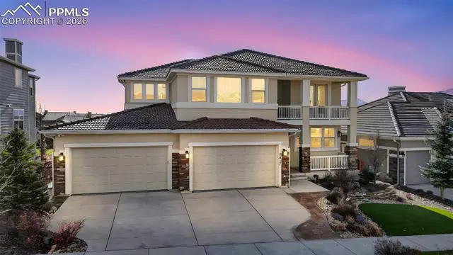 Two-story beige house with a brown roof, two-car garage, and a balcony, under a pink and purple sky.