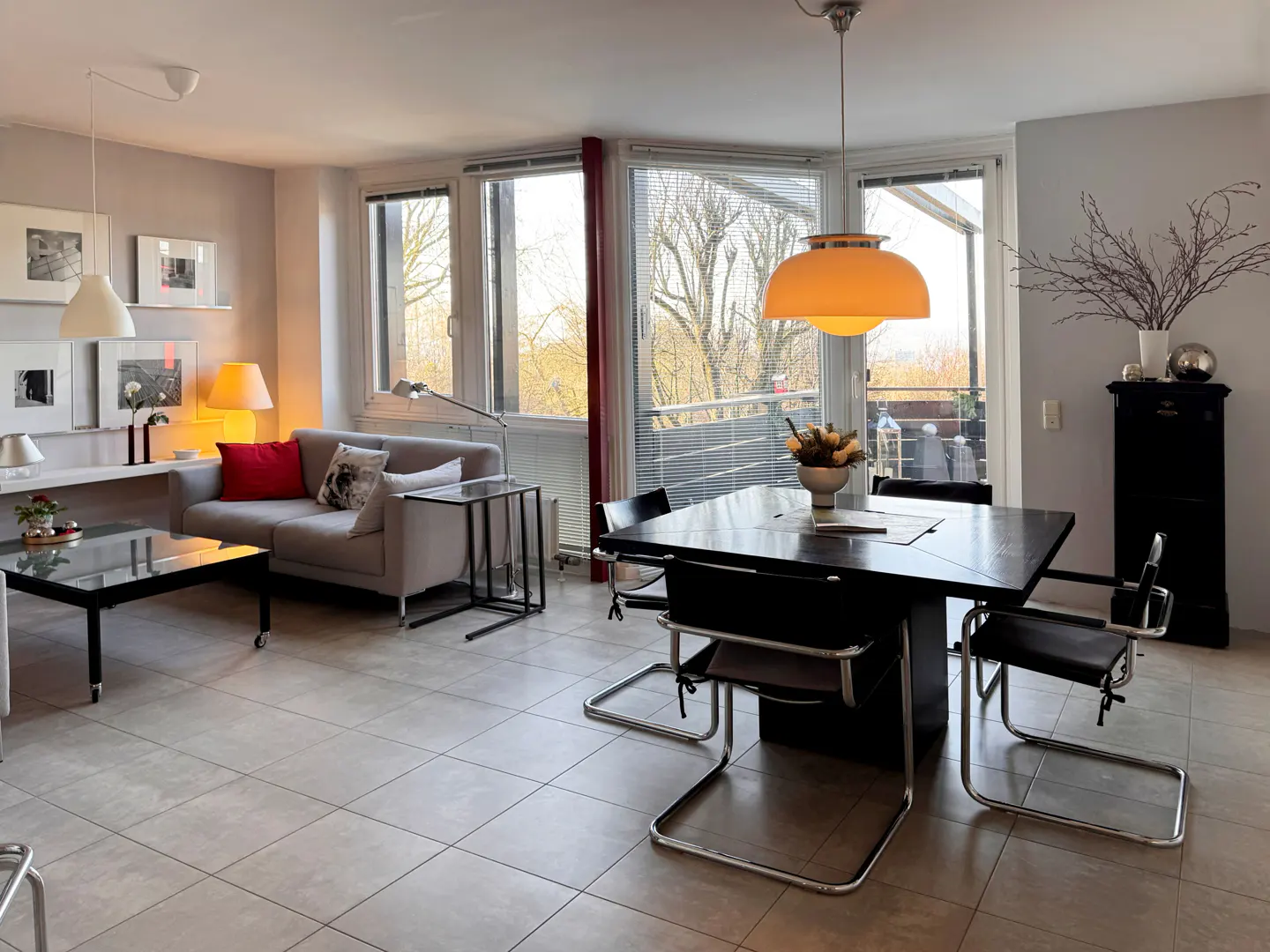 Living room with gray sofa, black table and chairs, and large windows with a view. An orange pendant light hangs above the table.