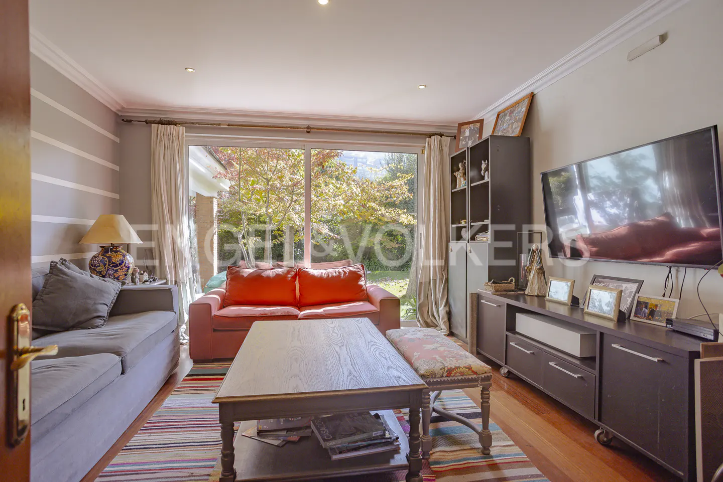 Living room with gray sofa, orange sofa, coffee table, TV, and view of the garden through a sliding glass door.