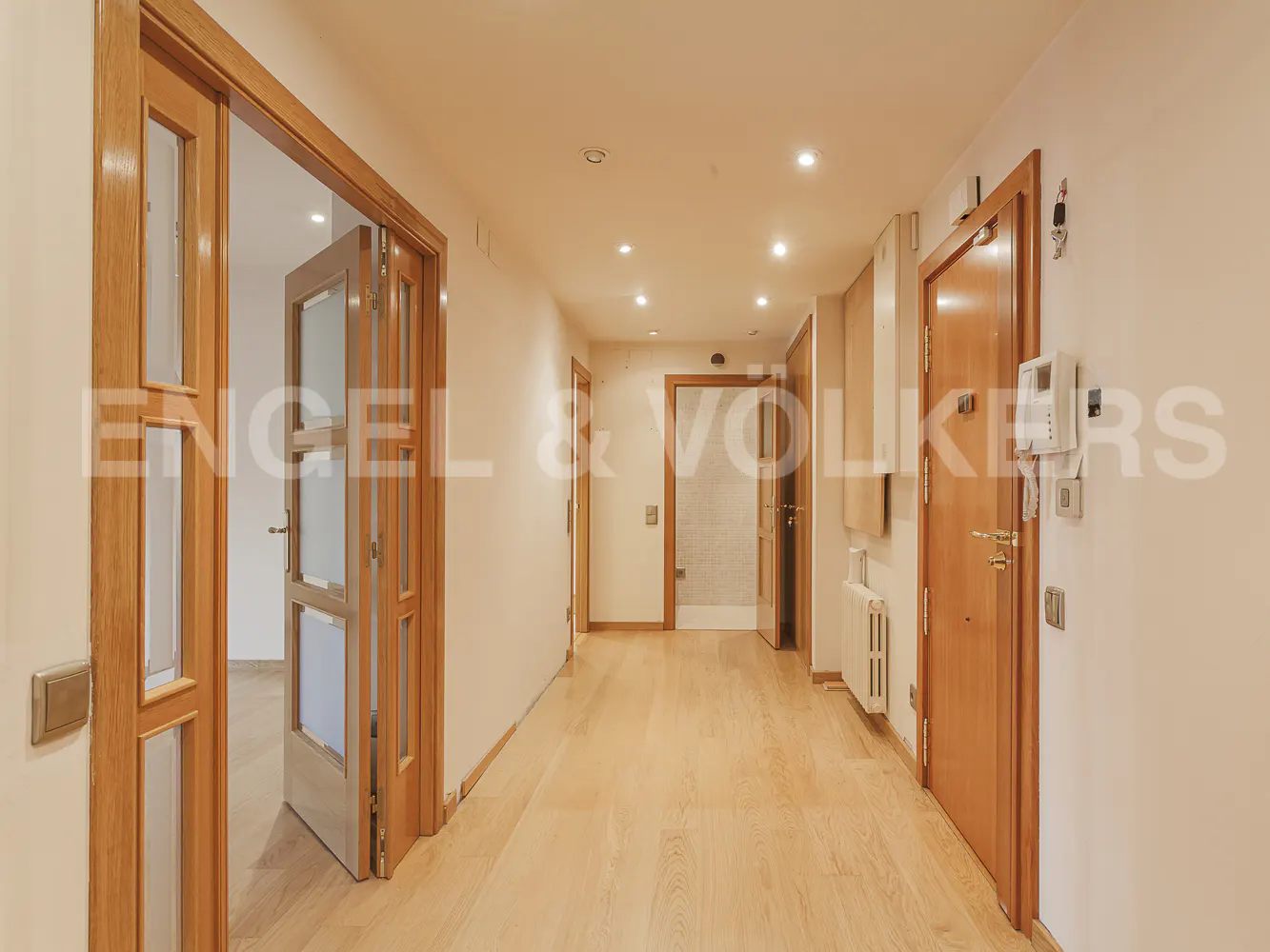 Bright hallway with light wood floors, white walls, and multiple wooden doors leading to other rooms in the home.