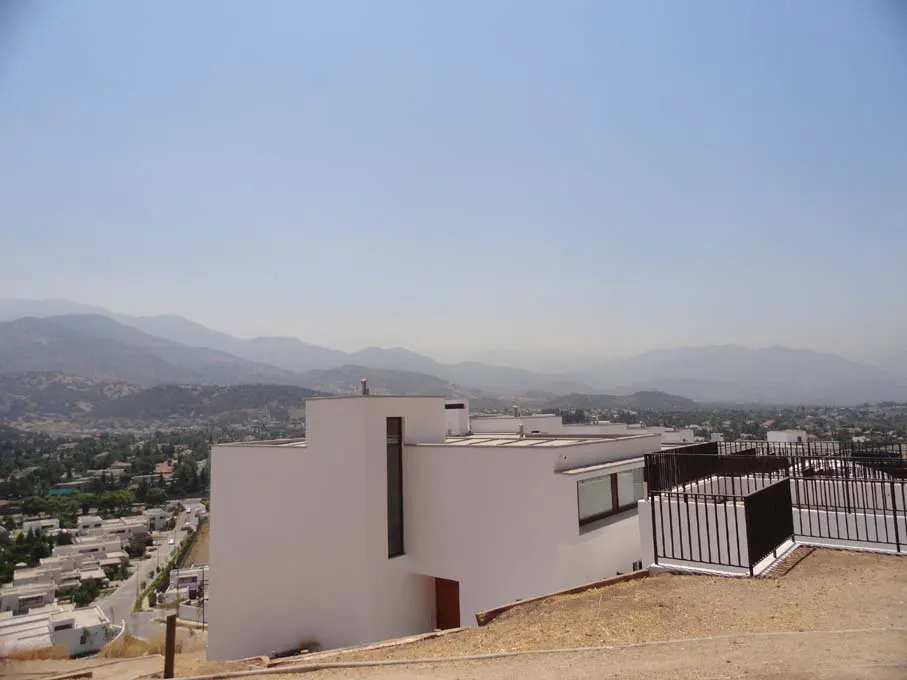 Modern white house on a hill overlooking a town and mountains under a clear blue sky.