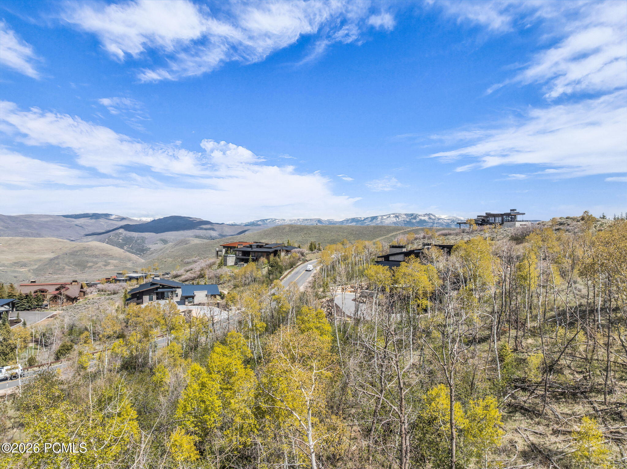Scenic view of luxury homes nestled in a hillside with autumn trees under a blue, cloudy sky. Mountains are visible in the distance.
