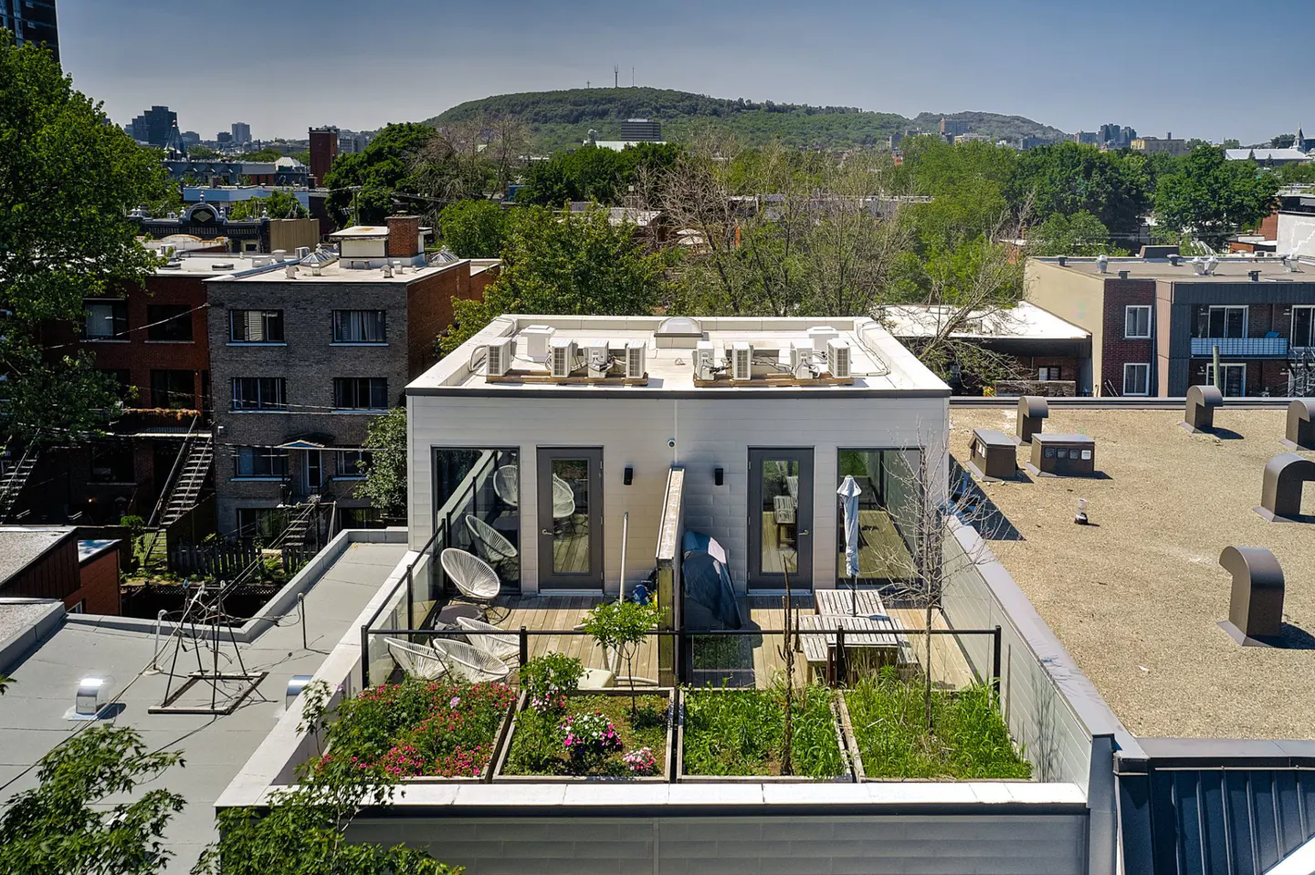 Rooftop view of a modern home with a garden, patio furniture, and a city skyline with a green mountain in the background.
