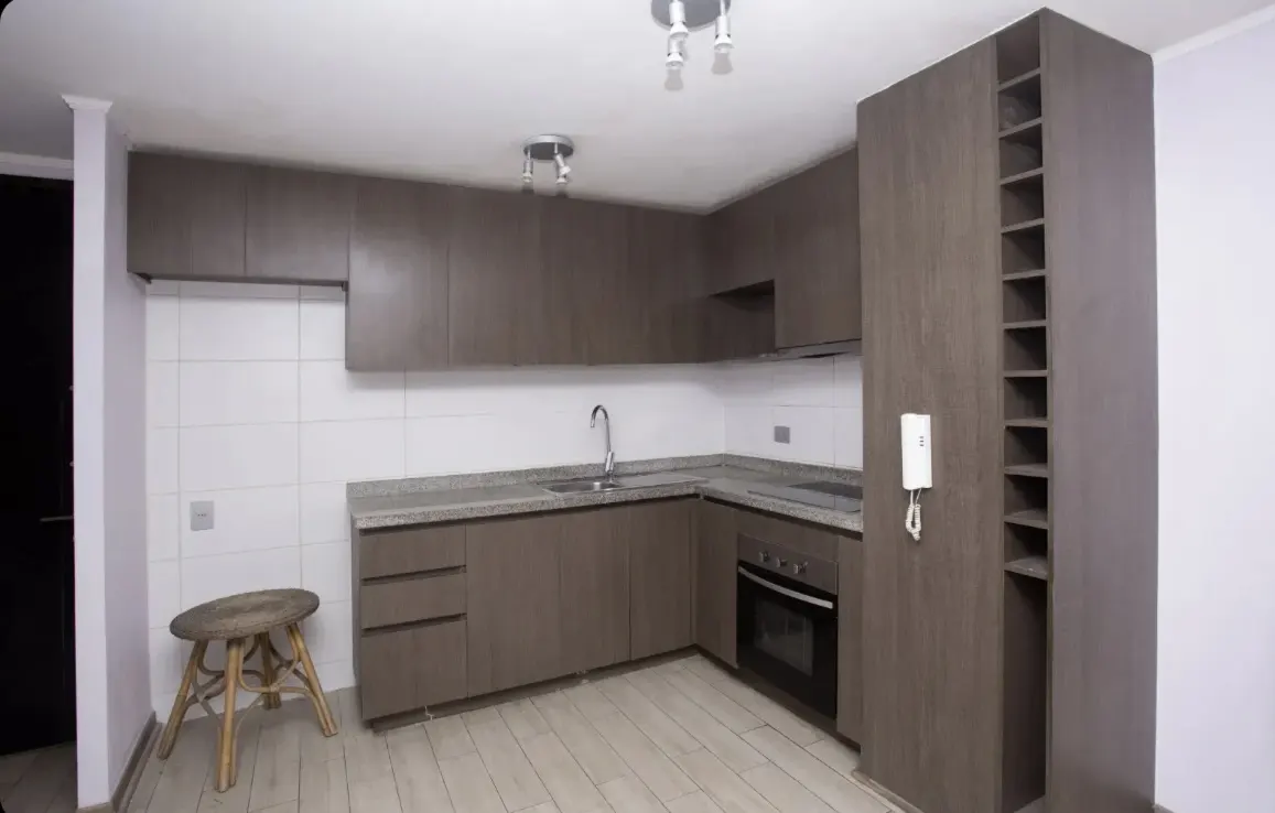 A modern kitchen with gray cabinets, granite countertops, and white tiled backsplash. A small wooden stool sits in the corner.