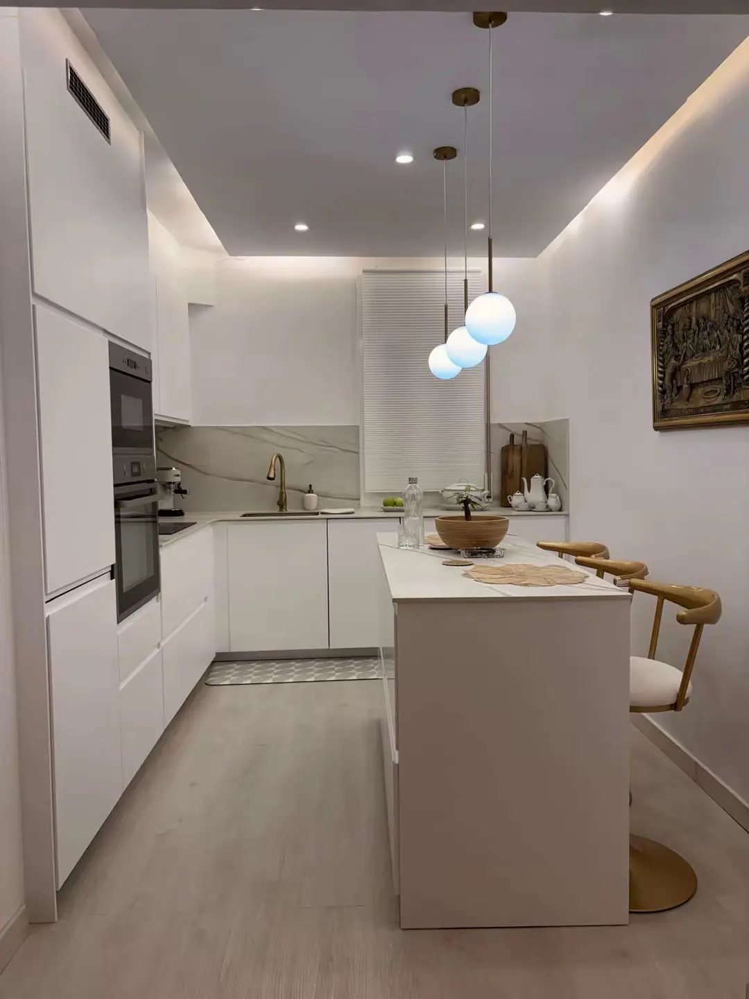 Bright, modern kitchen with white cabinets, marble backsplash, and island with bar stools. Three pendant lights hang above the island.