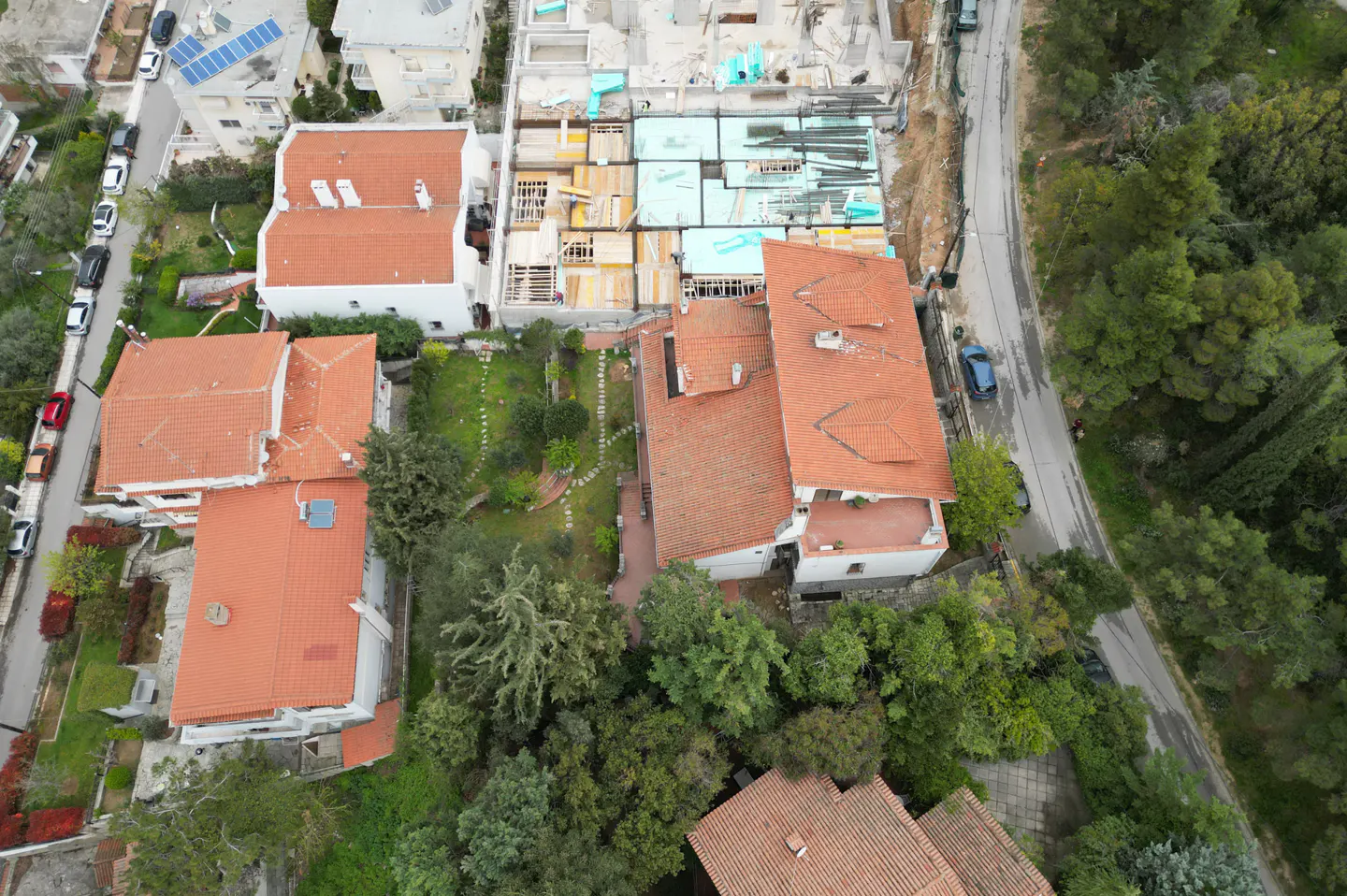 Aerial view of houses with red tile roofs, green trees, and a construction site in the background.