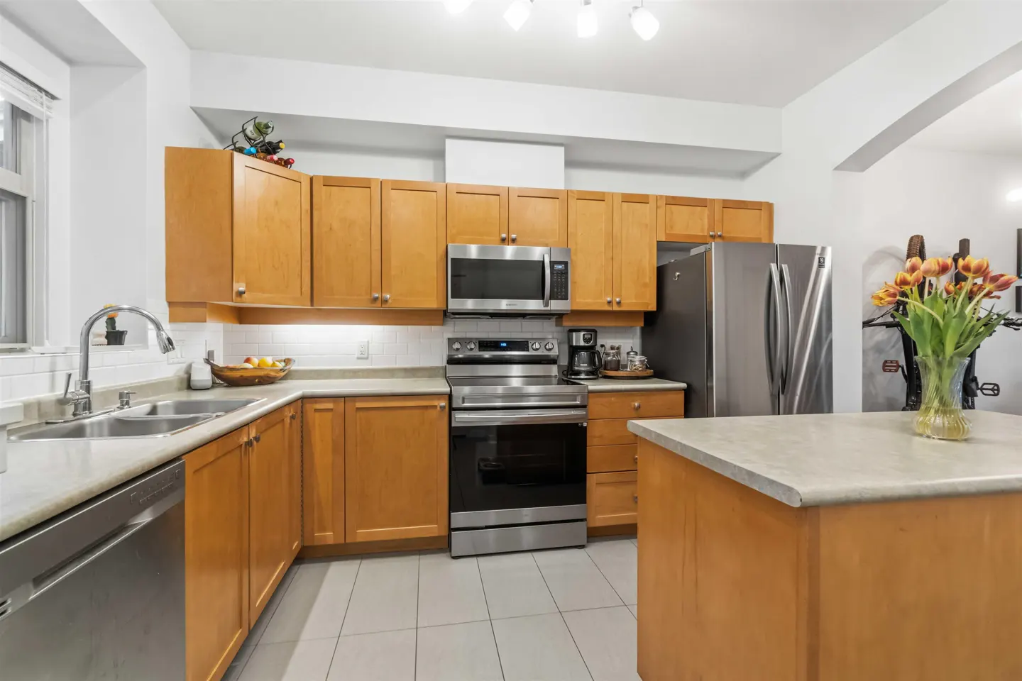 Bright kitchen with light wood cabinets, stainless steel appliances, and a center island topped with a vase of orange tulips.
