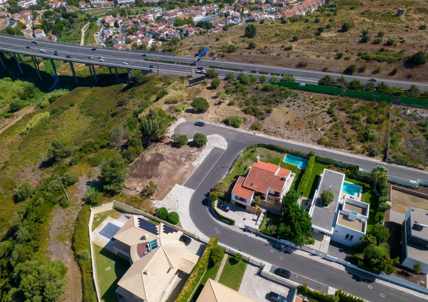 Aerial view of a suburban neighborhood with houses, swimming pools, and a nearby highway overpass.