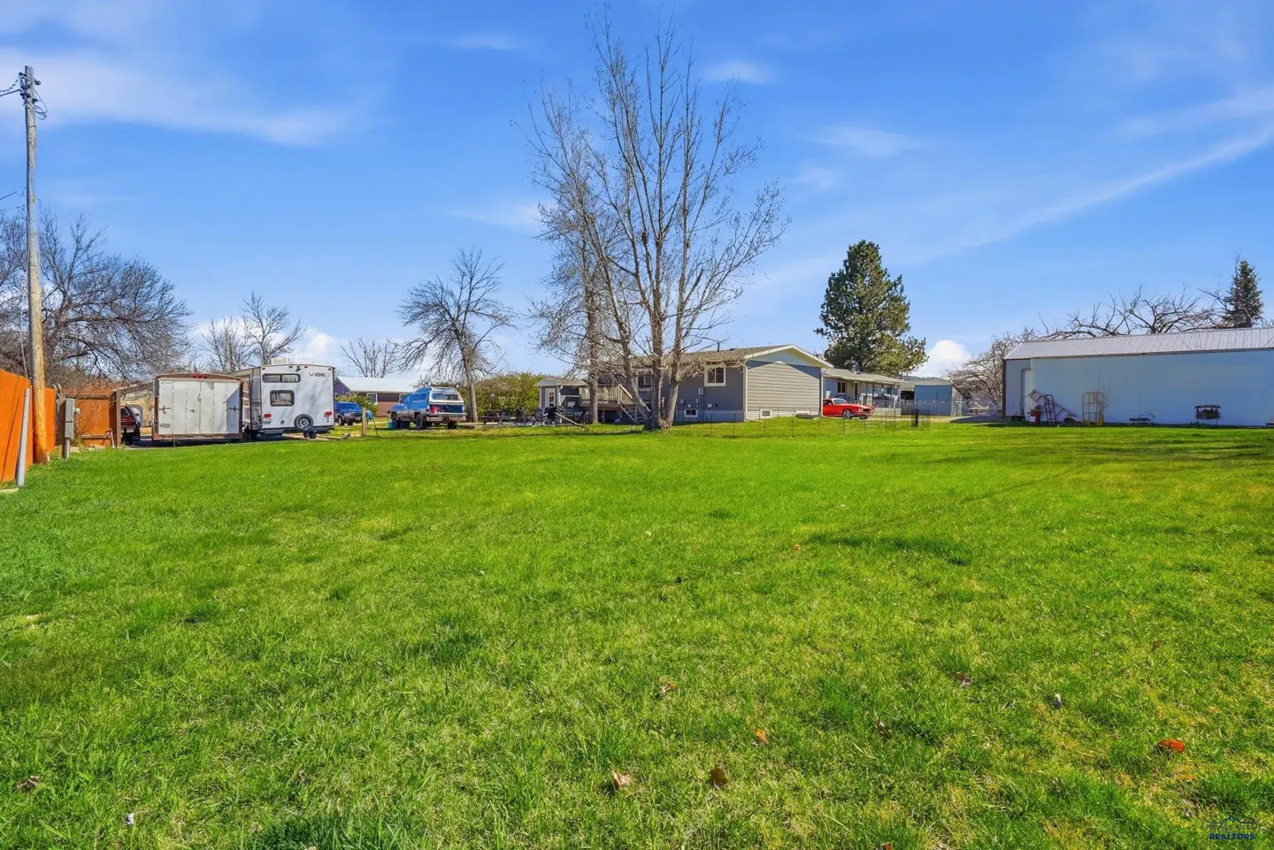 A wide shot of a large green lawn with a house, garage, and vehicles in the background under a blue sky.