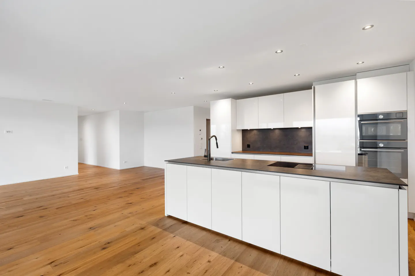 Bright, modern kitchen with white cabinets, dark countertops, and wood floors. Recessed lighting illuminates the space.