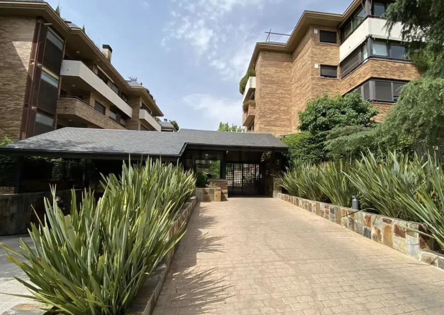 Exterior view of a brick apartment complex with a covered entrance and lush green landscaping.