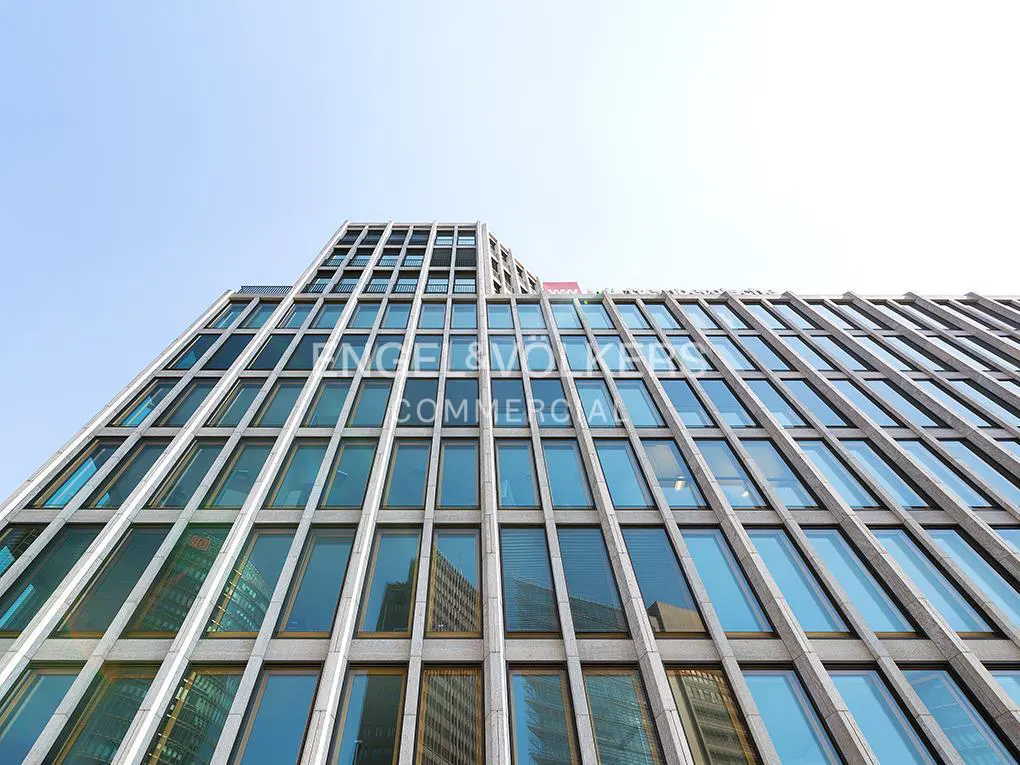 Low-angle view of a modern office building with a grid of glass windows reflecting the sky and surrounding architecture.