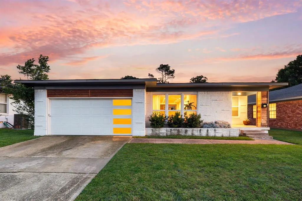 A white brick ranch-style house with a white garage door with yellow accents at dusk.