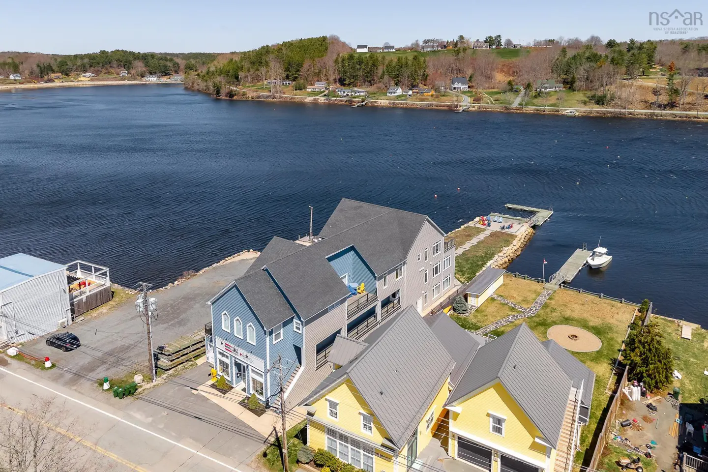 Aerial view of waterfront property with blue, gray, and yellow buildings, docks, and a boat on a sunny day.