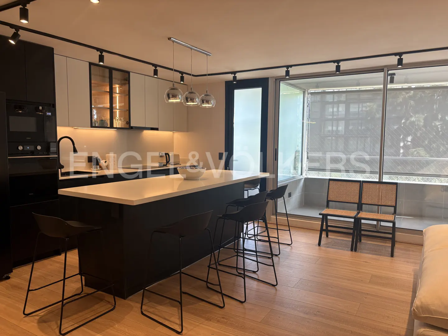 A modern kitchen with black cabinets, a white countertop island with black stools, and a window with two chairs.