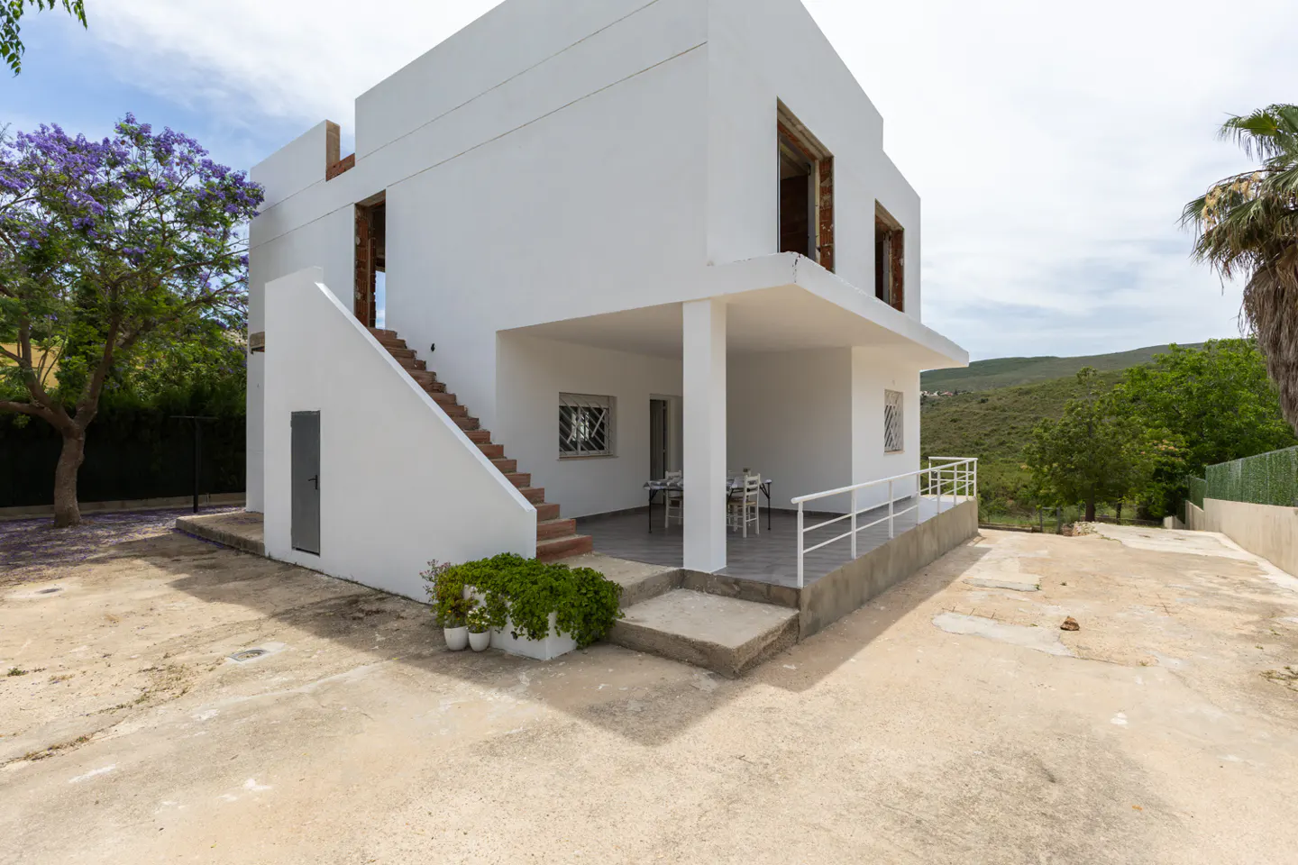 Modern white two-story house with an exterior staircase, covered patio, and scenic hillside views.