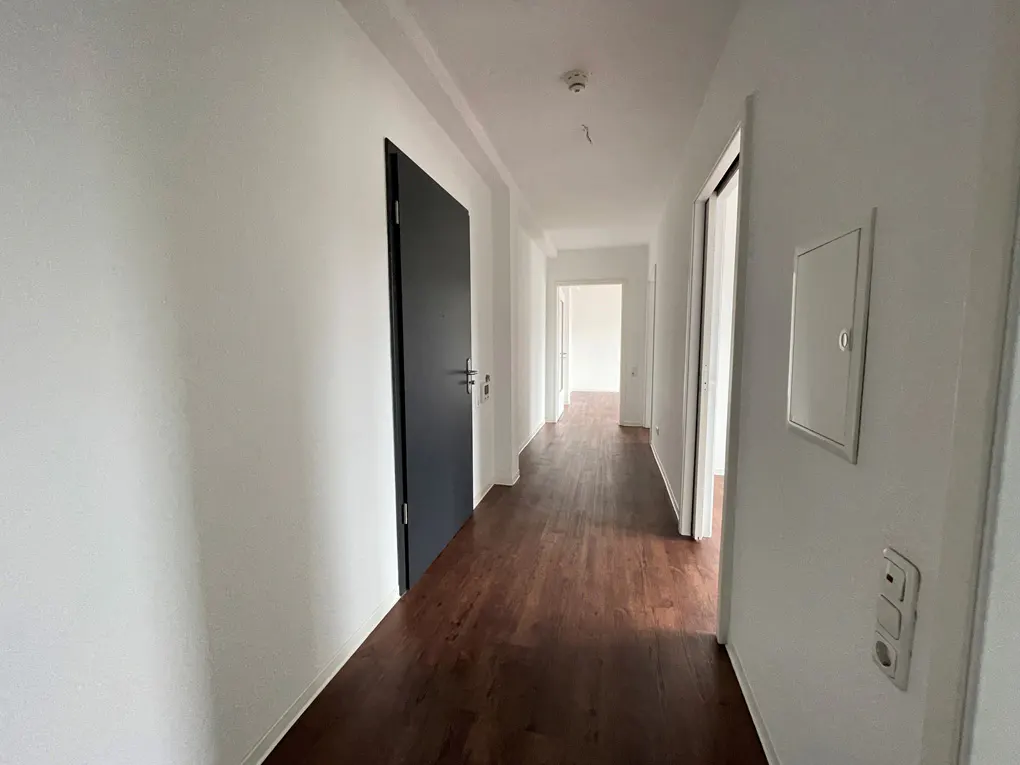 Hallway with dark wood floors and white walls. A black door is on the left. A white door is on the right.