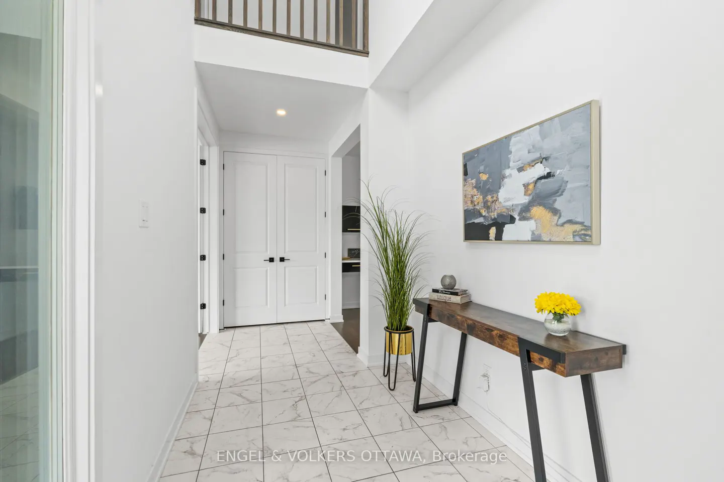 Bright foyer with white walls, marble tile floor, and a dark wood console table with yellow flowers. An abstract painting hangs above the table.