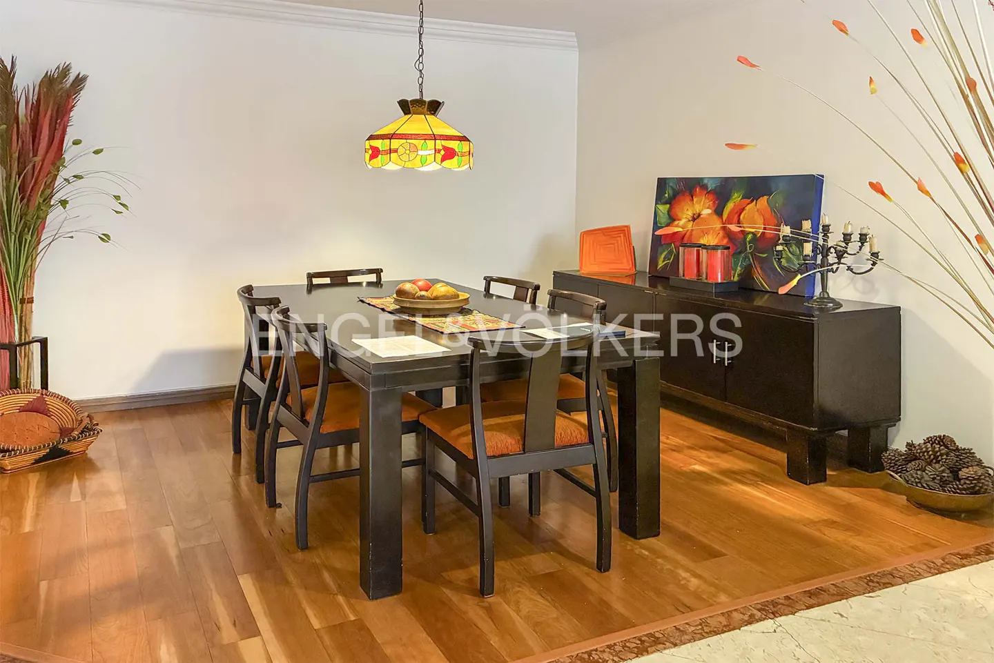 Dining room with a dark wood table, orange chairs, and a stained glass pendant light. A dark wood sideboard is against the wall.