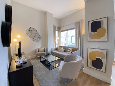 Living room with a gray sofa, two armchairs, a black TV stand, and abstract art on the walls.