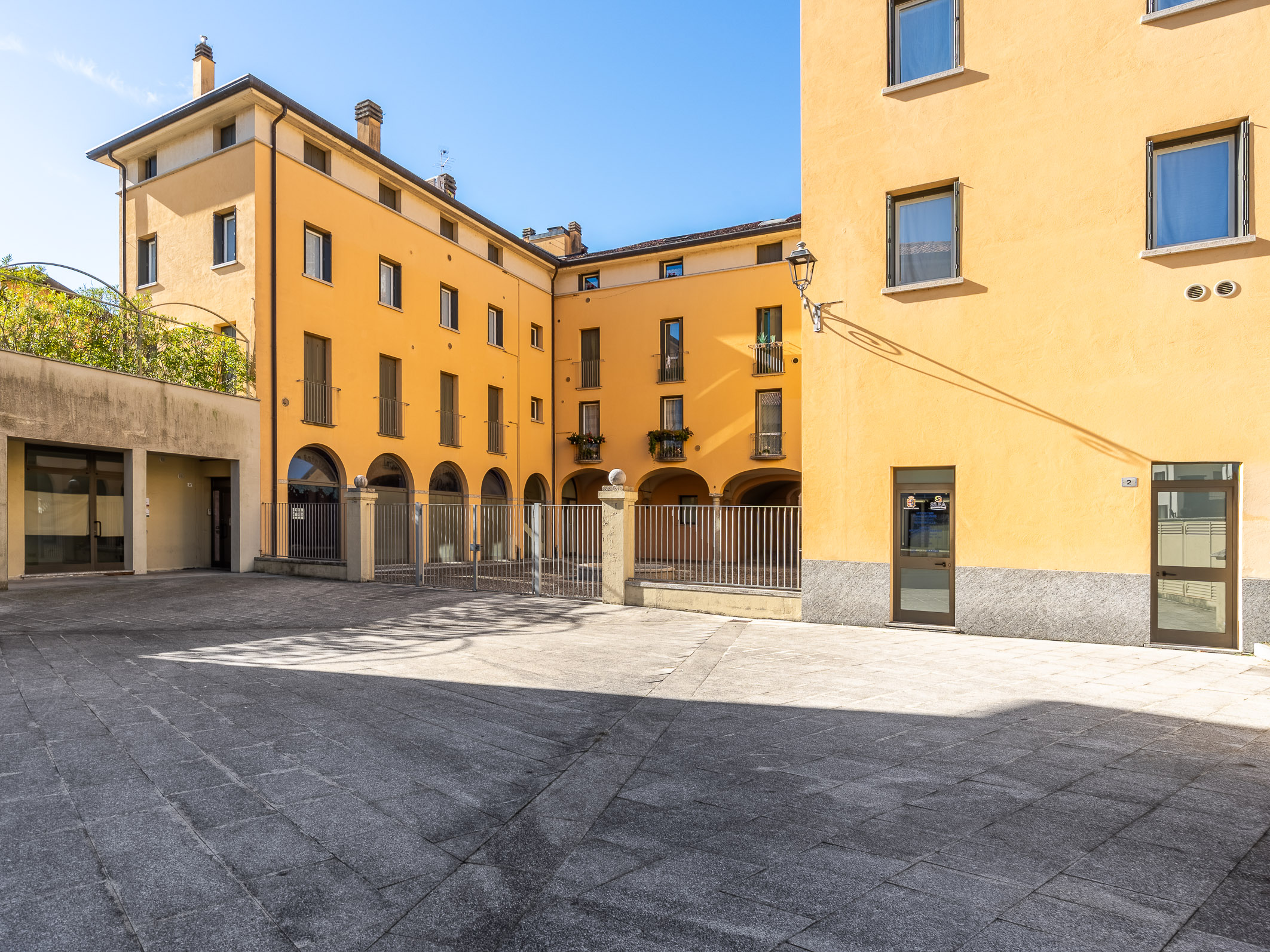 Courtyard view of a yellow apartment building with arched walkways and a gray stone paved ground. [AI-generated text]