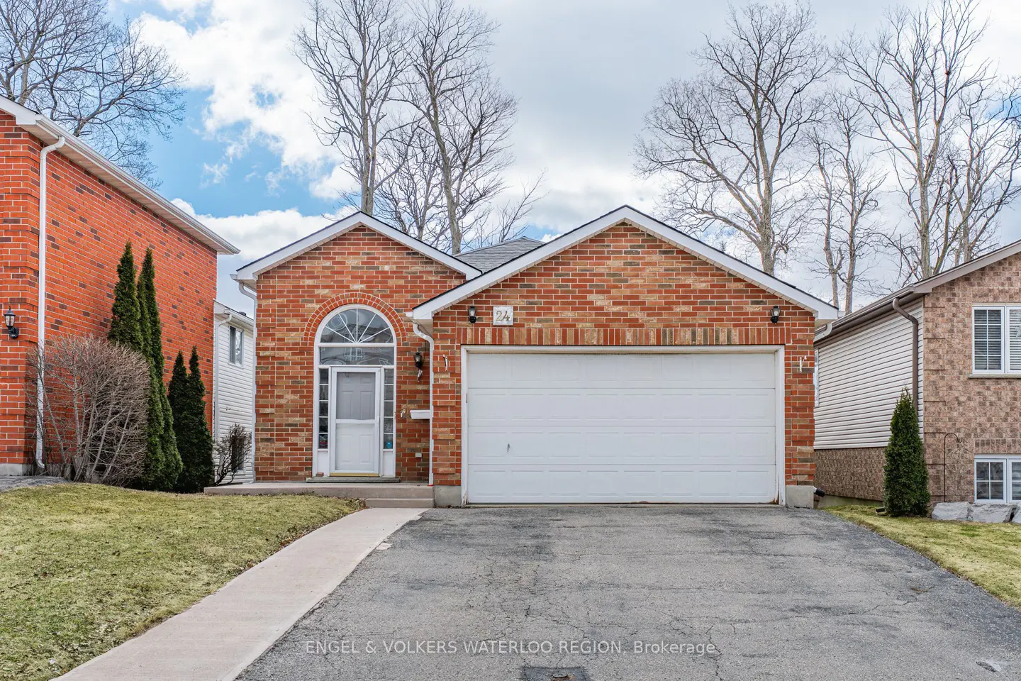 A single-story red brick house with a white garage door and front door. A paved driveway leads to the garage.