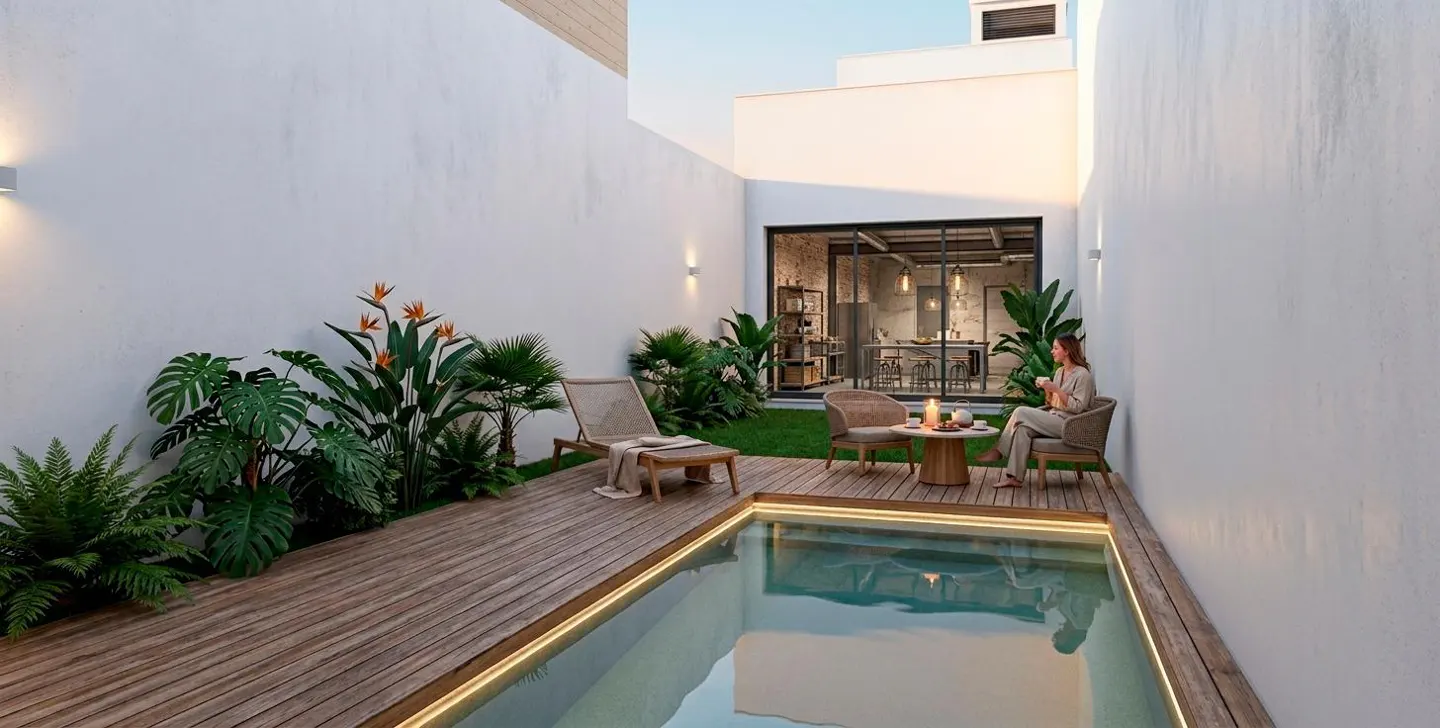 A modern backyard with a small pool, wooden deck, and white walls. A woman sits at a table with chairs, and a lounge chair is nearby. Tropical plants add greenery.